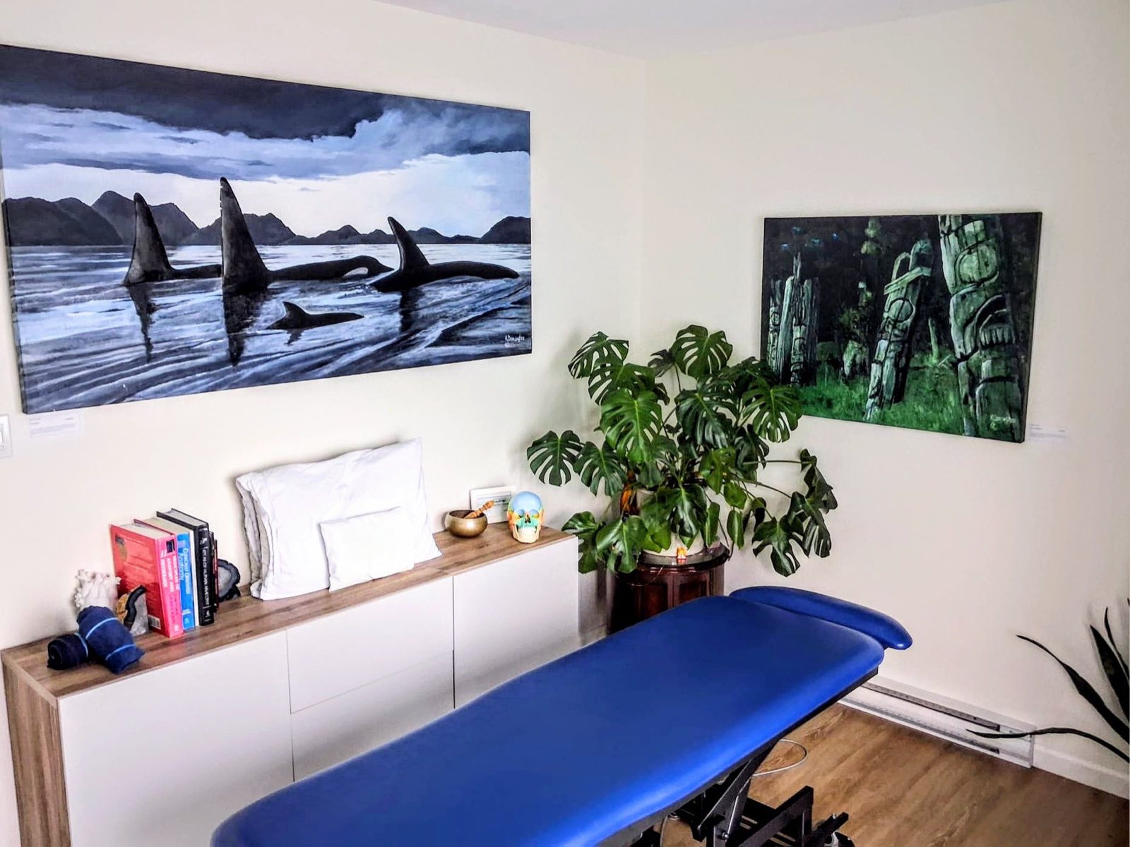 A treatment room with a table made up and artwork on the wall.