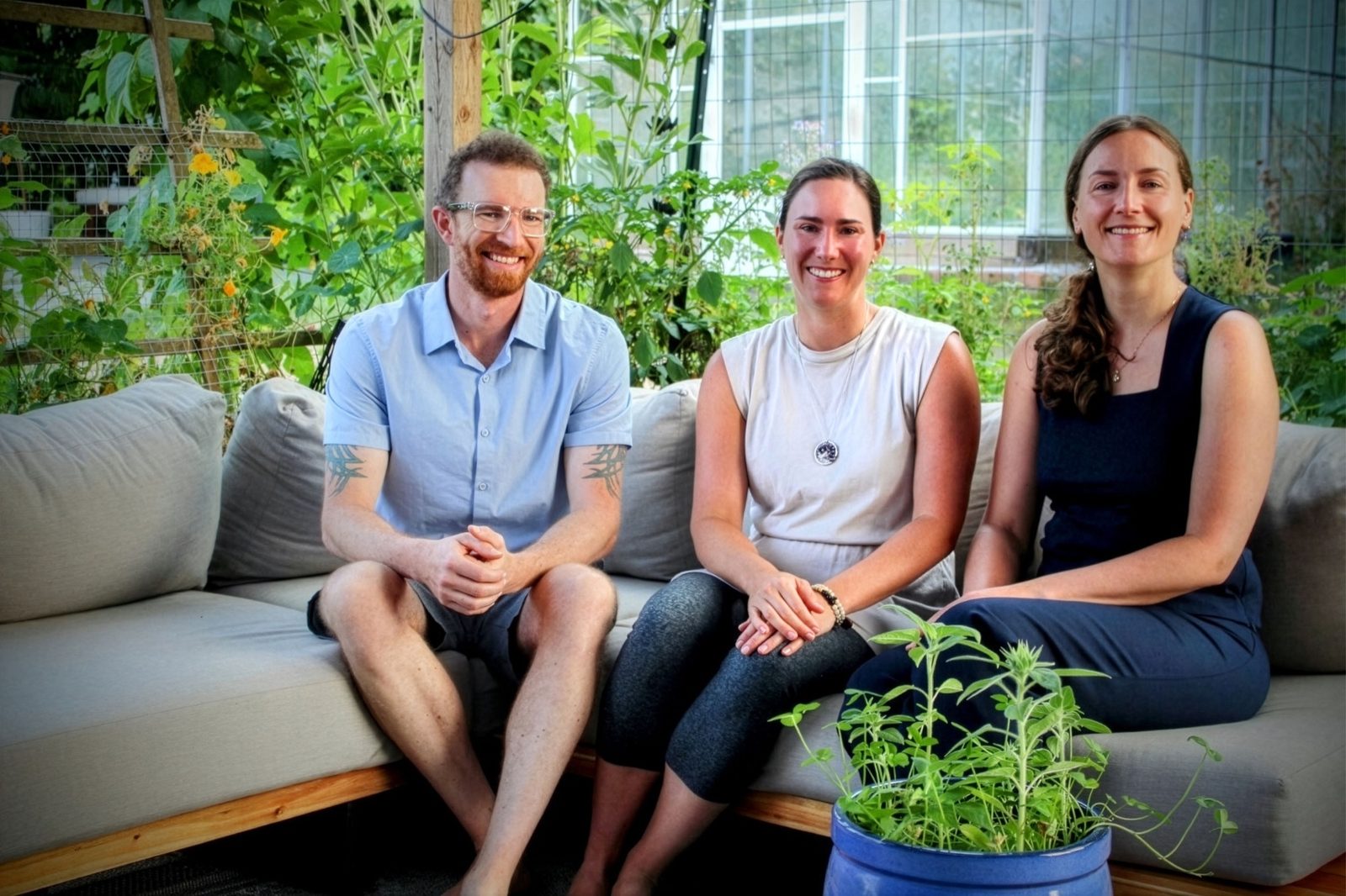 James Boyce, Kayla Larsen, and Erin Chaba sitting together on a couch in a garden, smiling.