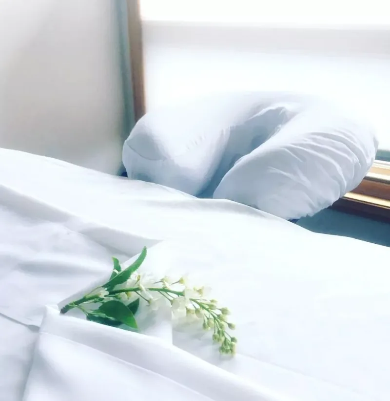 Close-up of fresh white linens and a face cradle on the massage table at Multidimensional Health, with a sprig of white flowers in soft natural light.